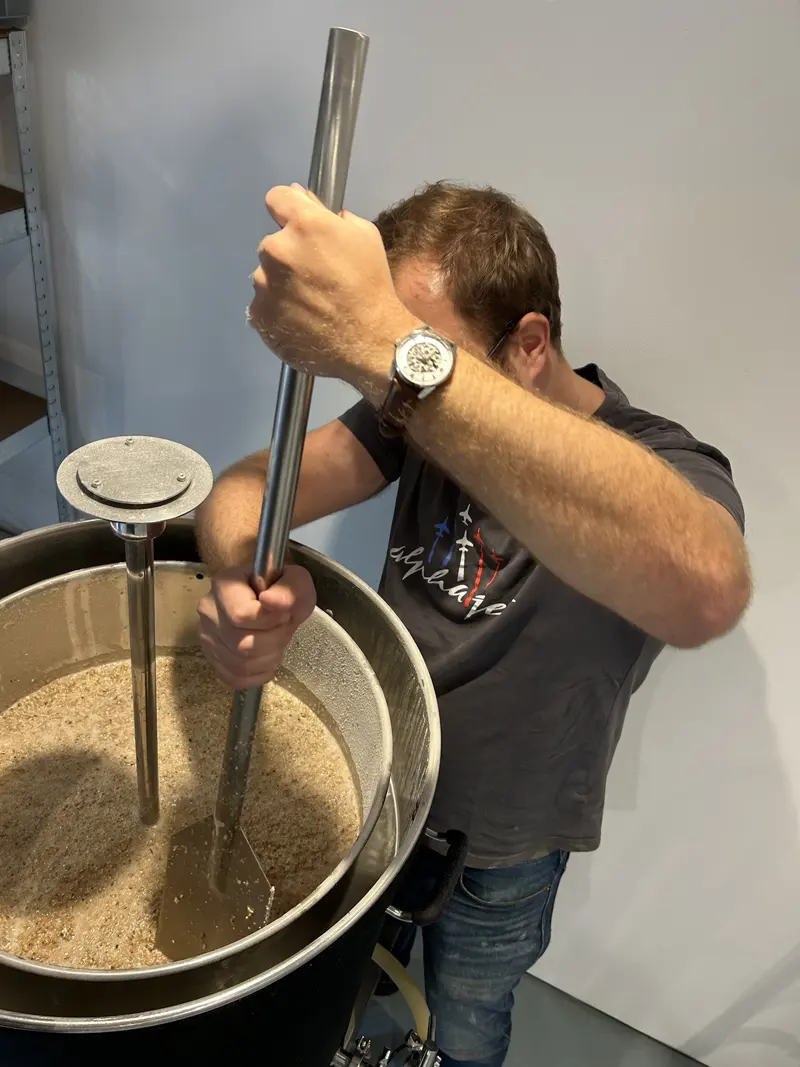 Un homme remue le grain avec une longue pagaie d'acier dans la cuve de brassage.